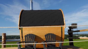 A wooden cabin with a chimney, two Adirondack chairs, and a rope barrier.