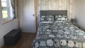 A bedroom with a bed, a window, a door, and a bench. - The Snuggly Sheep Shepherd Hut & Sauna Farm Stay (Ballyshannon)