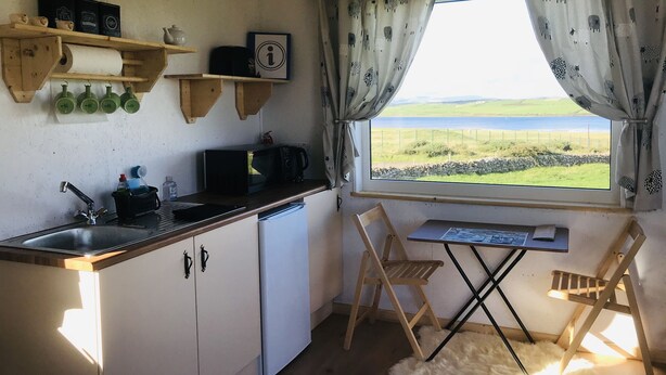 A compact kitchen with a view of the sea, a wooden table, and a chair. - The Snuggly Sheep Shepherd Hut & Sauna Farm Stay (Ballyshannon)