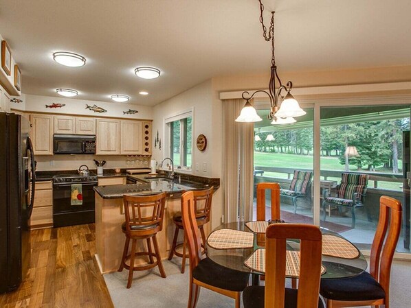 Una cocina con armarios de madera, una isla central y una zona de comedor con sillas y mesa.