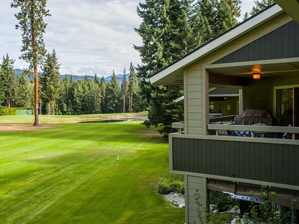 A house with a balcony overlooking a well-maintained lawn and a golf course.