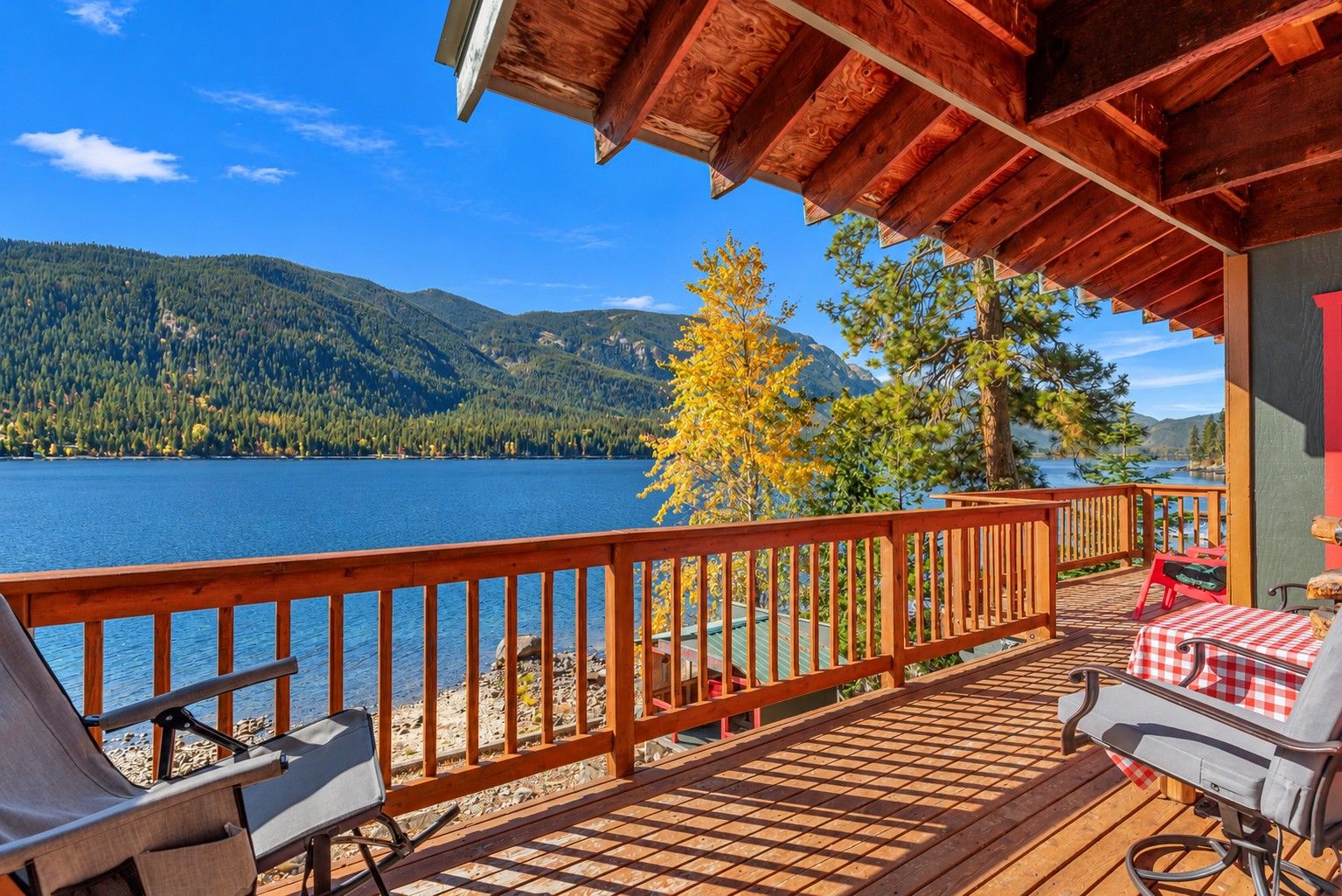 A wooden deck with a view of a lake and mountains, outdoor seating, and a covered area with a table and chairs.