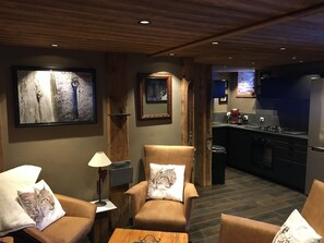 A modern living room with leather armchairs, a coffee table, and a fireplace. A kitchen is visible in the background with modern appliances. - Cosy apartment in a quiet, authentic chalet (Vallorcine)