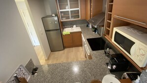A compact kitchen with a refrigerator, microwave, sink, and wooden cabinets. - Private property in front of Boadella beach (Lloret de Mar)