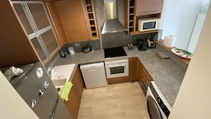 A compact kitchen with wooden cabinets, a microwave, a stove, and a dishwasher. - Private property in front of Boadella beach (Lloret de Mar)
