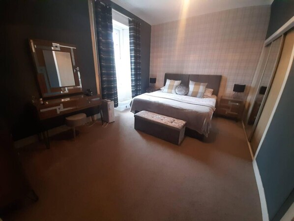 A bedroom with a bed, a dresser, a mirror, and a window with curtains. - Stunning Riverside Town House With Views, Ayrshire (Girvan)