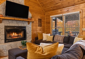 A cozy living room with a fireplace, comfortable seating, and a large window with blinds.