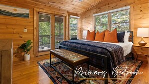 A primary bedroom with wooden walls, a bed with blue bedding, orange pillows, a bench, and a ceiling fan. - TreeHouse Vibe • Slide, Swings, Rock Wall • HotTub • FirePit • Games • Secluded (Blue Ridge)