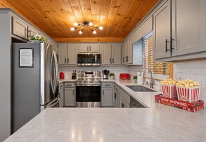 A modern kitchen with stainless steel appliances, a wooden ceiling, and a pop corn box on the counter. - Enchanted Hideaway: TreeHouse • Slide • HotTub • FirePit • Fun Games • Secluded (Blue Ridge)