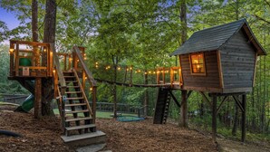 A treehouse with a wooden staircase and a slide, surrounded by a forest. - TreeHouse Vibe • Slide, Swings, Rock Wall • HotTub • FirePit • Games • Secluded (Blue Ridge)