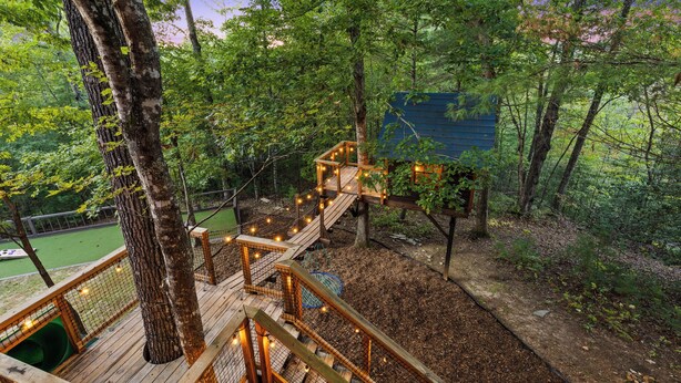 A wooden deck with a rope bridge connecting to a treehouse, surrounded by dense forest. - TreeHouse Vibe • Slide, Swings, Rock Wall • HotTub • FirePit • Games • Secluded (Blue Ridge)