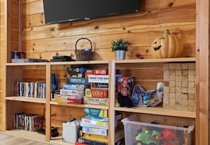 A wooden interior with shelves holding board games, a television, and a pumpkin decoration.