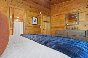A wooden cabin room with a bed, a dresser, a mirror, and a framed picture on the wall.
