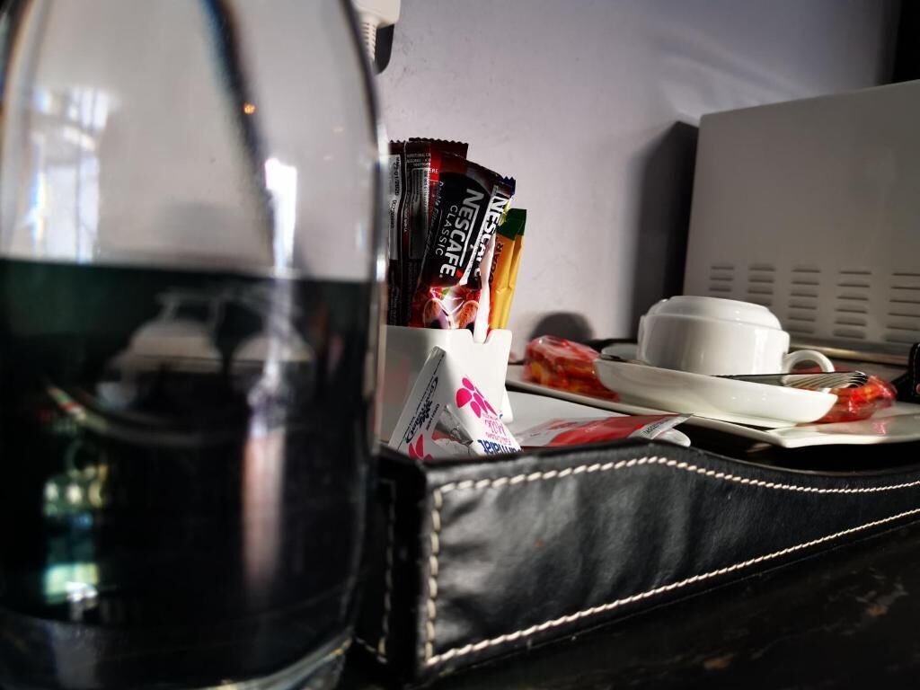 A coffee maker, a cup, a plate with food, and a bag of Nescafe Classic coffee packets on a table.