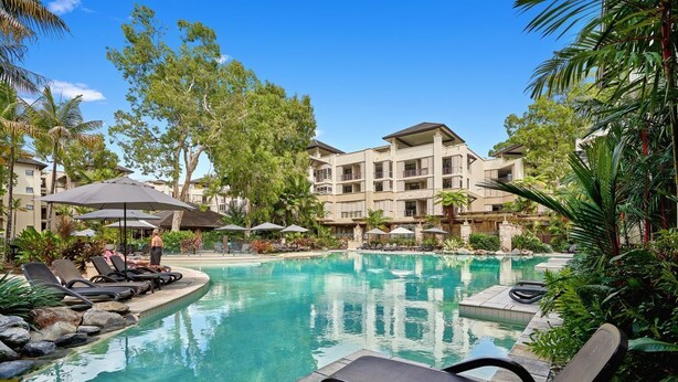 A pool area with lounge chairs, umbrellas, and a building with multiple balconies. - 2 Bedroom 2 Bathroom Swim Out Apartment in the Temple resort Palm Cove (Palm Cove)