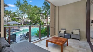 A balcony with a pool view, a wooden table, and wicker furniture. - 2 Bedroom 2 Bathroom Swim Out Apartment in the Temple resort Palm Cove (Palm Cove)