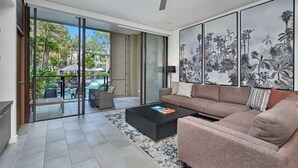 A modern living room with a large sofa, a coffee table, and a view of a pool and outdoor area through glass doors. - 2 Bedroom 2 Bathroom Swim Out Apartment in the Temple resort Palm Cove (Palm Cove)