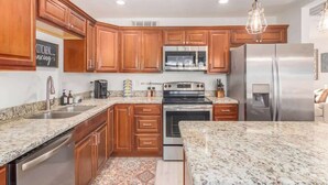 A kitchen with wooden cabinets, stainless steel appliances, granite countertops, and pendant lighting.