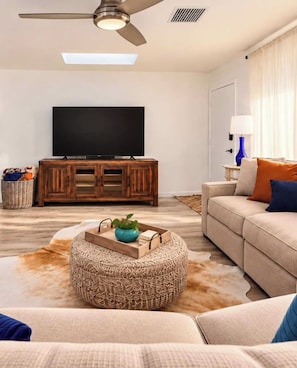 A living room with a flat-screen TV, wooden cabinet, sofa, ottoman, and a ceiling fan. - The Eldorado | Two Masters | Pool + Hottub | Mural (Scottsdale)