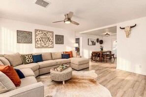 A modern living room with a sectional sofa, a round coffee table, and a dining area with a wooden table and chairs.