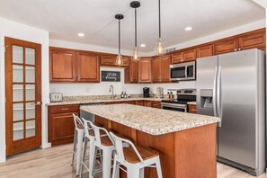A modern kitchen with wooden cabinets, a stainless steel refrigerator, a granite countertop, and pendant lighting.