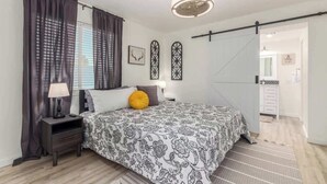 Een slaapkamer met een bed, nachtkastje, lamp, gordijnen en een plafondventilator.