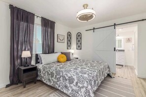 Une chambre à coucher avec un lit, une table de chevet, une lampe, des rideaux et un ventilateur de plafond.