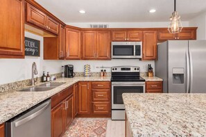 A kitchen with wooden cabinets, stainless steel appliances, granite countertops, and a decorative sign. - The Eldorado | Two Masters | Pool + Hottub | Mural (Scottsdale)