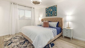 A bedroom with a bed, bedside tables, a ceiling light, a window with curtains, and a painting on the wall.