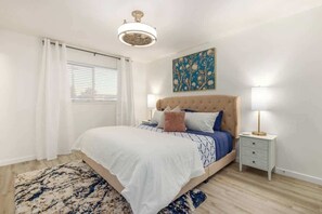 Una camera da letto con un letto, comodini, una lampada a sospensione, una finestra con tende e un quadro appeso al muro.