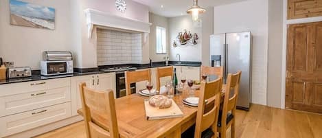 A modern kitchen with white cabinets, a wooden dining table, and a stainless steel refrigerator.