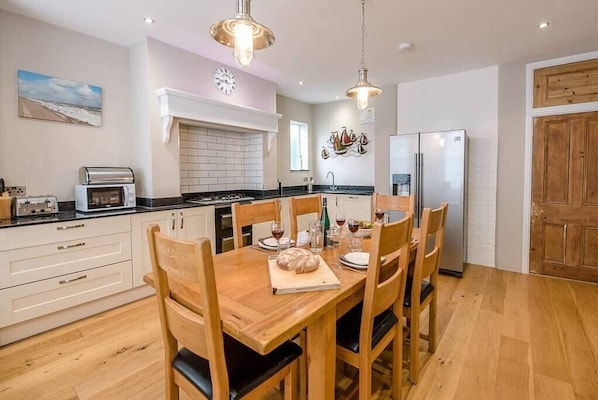 A modern kitchen with white cabinets, a wooden dining table, and a stainless steel refrigerator. - 4 Market Cross House, Aldeburgh (Aldeburgh)