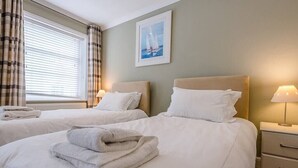A hotel room with two beds, a window with curtains, a painting on the wall, and a bedside table with a lamp. - 4 Market Cross House, Aldeburgh (Aldeburgh)