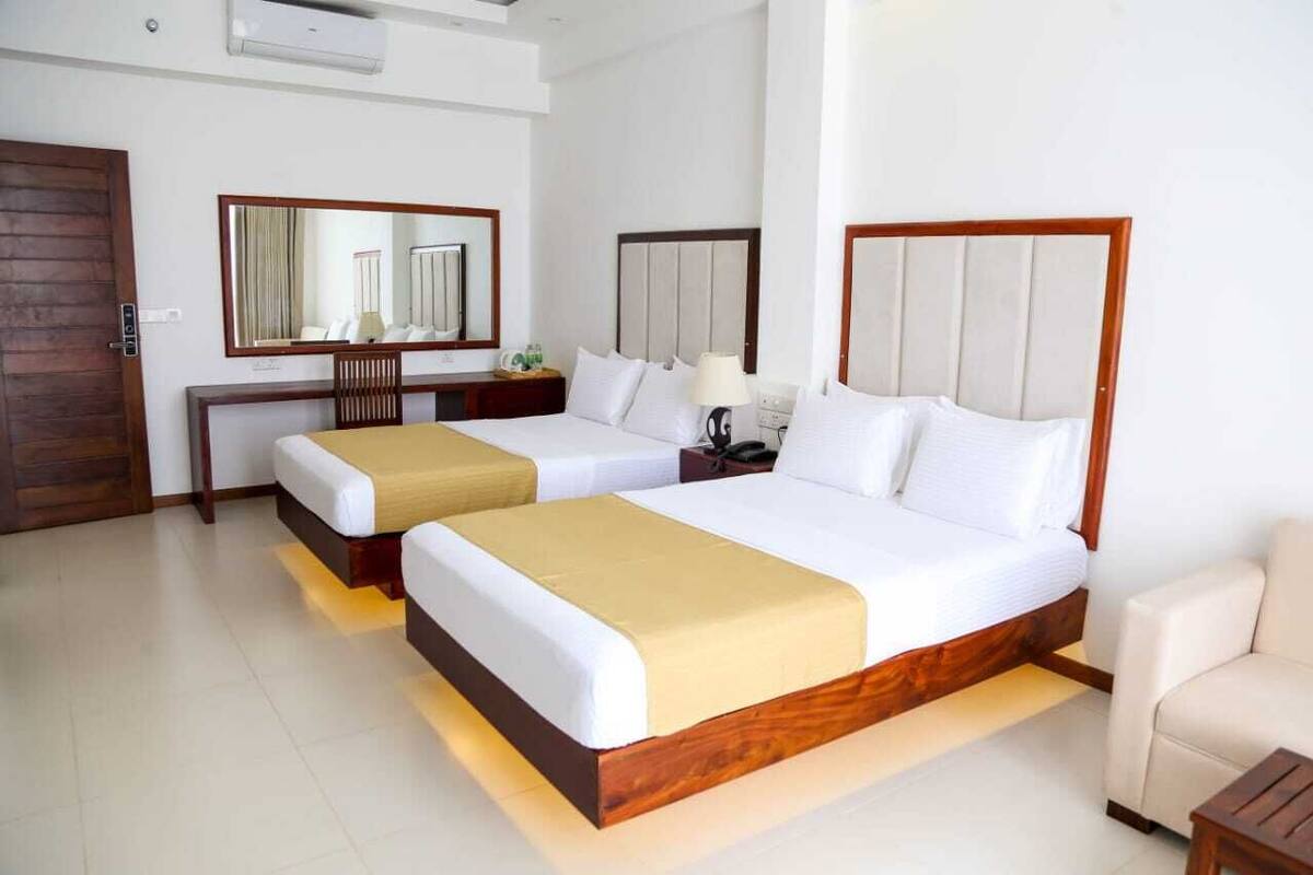 A hotel room with two beds, a wooden headboard, a bedside table with a lamp, a mirror, and a wooden door.