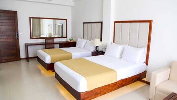 A hotel room with two beds, a wooden headboard, a bedside table with a lamp, a mirror, and a wooden door.