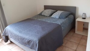 A single bed with a grey headboard and patterned bedding in a room with white walls and a tiled floor. - Appartement piscine (Mouans-Sartoux)
