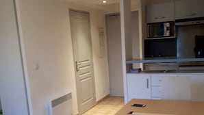A small, modern kitchen with white cabinets, a microwave, and a coffee machine. There is a dining table with two chairs in the foreground. - Appartement piscine (Mouans-Sartoux)
