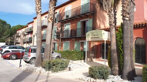 A multi-story hotel with balconies, parked cars, and palm trees. - Appartement piscine (Mouans-Sartoux)