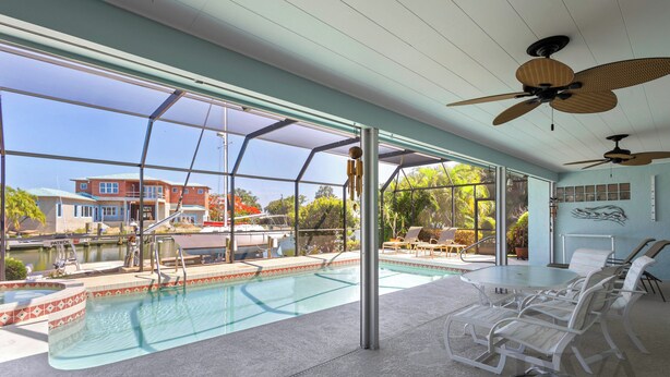 Un espace piscine offrant une vue sur un quai et des bâtiments, un coin salon abrité et des ventilateurs de plafond.
