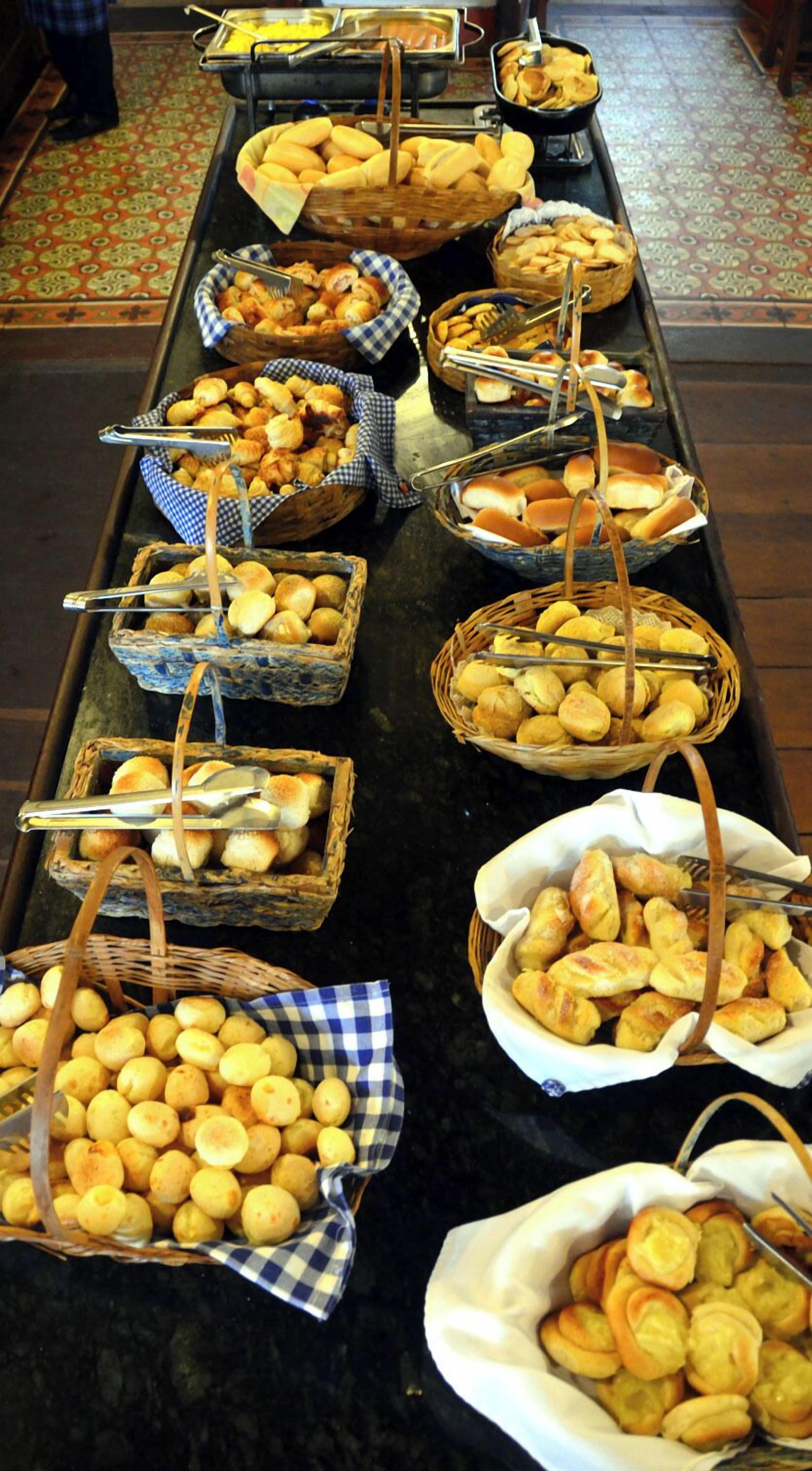 A buffet table with various baked goods, including bread rolls, pastries, and cookies, arranged in baskets and on trays.