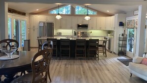 Una cocina moderna con armarios blancos, una isla central y una zona de comedor con sillas de madera.