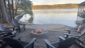 Terraza junto al lago con un brasero rodeado de sillas Adirondack, un anillo de fuego de piedra y vistas al lago.