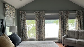 Un dormitorio con una cama grande, un sofá y vistas a un lago a través de las ventanas.