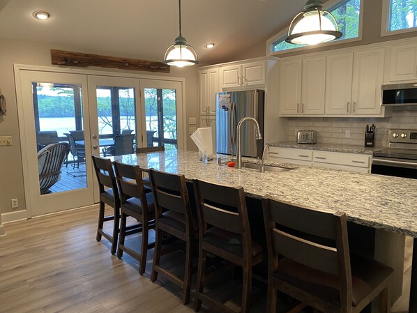 A kitchen with a large island, white cabinets, stainless steel appliances, and a view through the glass doors. - Mid-lake spacious cottage w/amazing views, deep water, protected swimming area. (Dadeville)