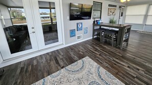 Amplia sala de estar con un televisor grande, piso de madera y ventilador de techo.