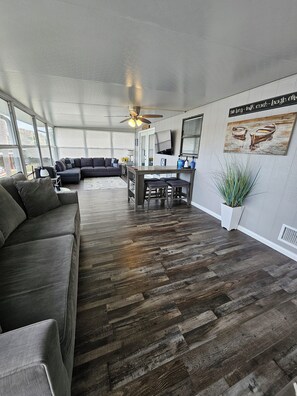 A spacious living area with a dark wood floor, a sectional sofa, a dining table with stools, and a ceiling fan. - Fishin' for Days! Waterfront Home with Covered Boat Dock in Okeechobee! (Okeechobee)