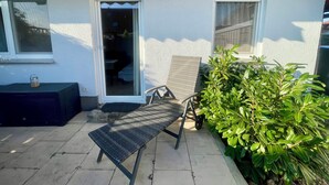 Une terrasse avec une chaise en métal, une petite table et un pot de fleurs.