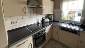 Une cuisine avec des armoires de couleur beige, un plan de travail noir, une cuisinière et une fenêtre donnant sur l’extérieur.