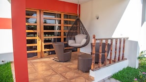 Un espacio exterior techado con una silla colgante, mobiliario de mimbre y una escalera de madera.