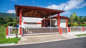 Un edificio de techo rojo y paredes blancas, rodeado por una valla blanca, con un paisaje verde de fondo.